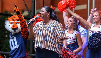 Octavia cheers into a microphone while Aubie and the cheerleaders cheer behind her