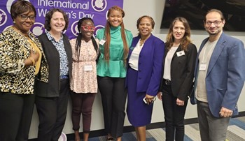 Group of faculty standing in front of International Women's Day sign