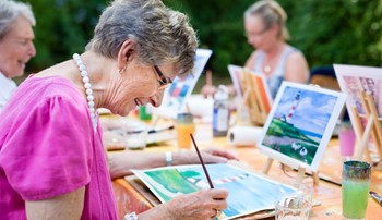 An older woman smiling as she paints with a group