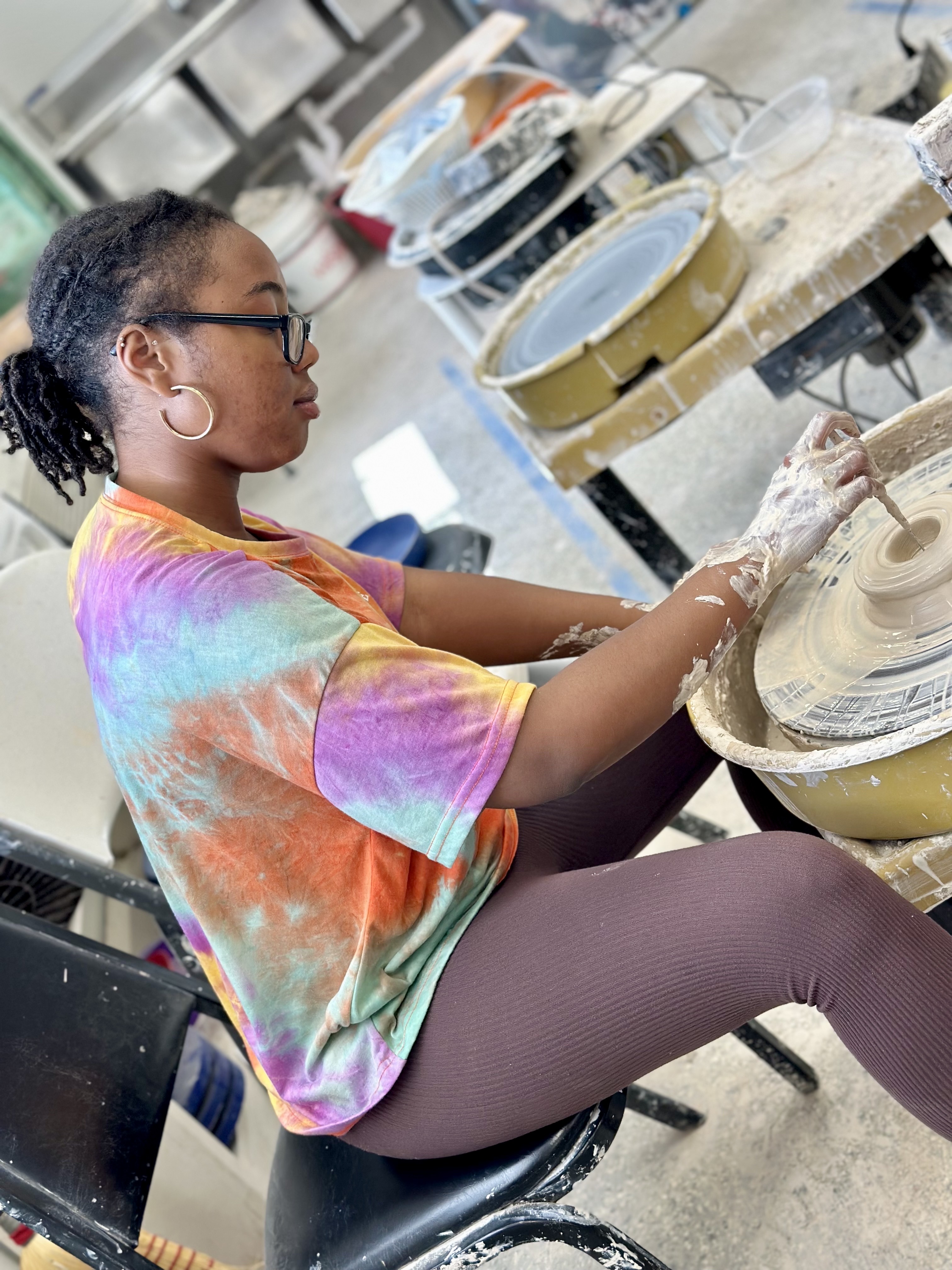 Kaitlin sits at a pottery wheel forming a sculpture