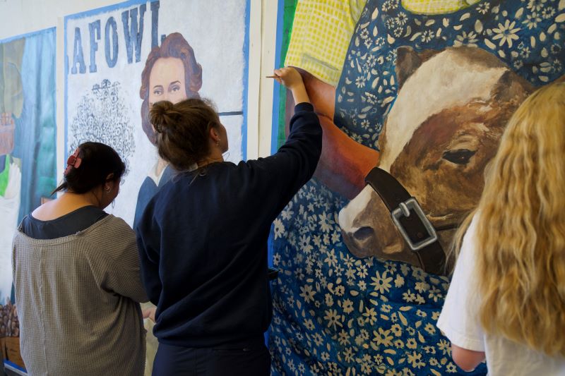 Three students painting part of agricultural mural