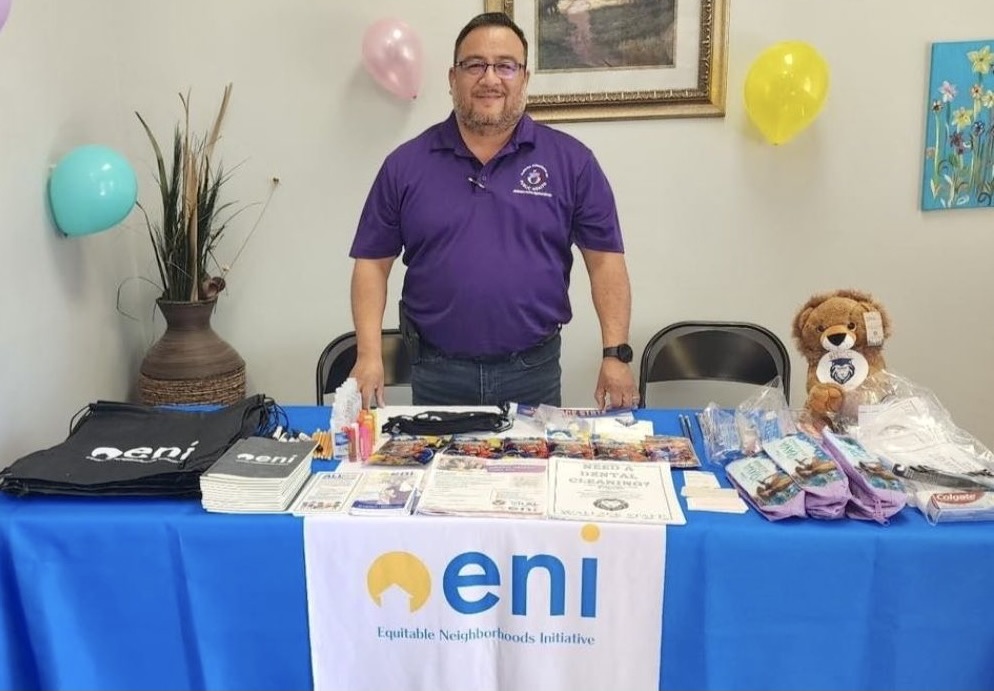 Greg Sarabia stands at an ENI table filled with literature and prizes