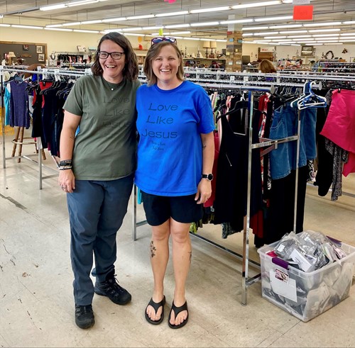 Jaxx Smith & Angela Bryan pose in front of a rack of clothing that Seeds of Faith thrift store