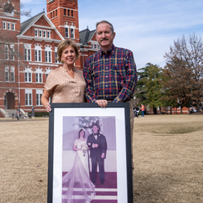 Dan and Marilyn Furlong stand in front of Samford Hall holding a photo from their wedding