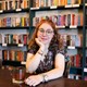 Louise Schulmann-Darsy sits at a cafe with a bookshelf of romance novels behind her