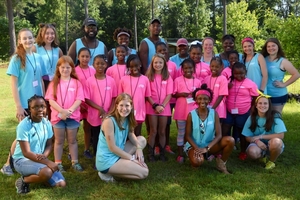 girls in pink and blue shirts stand together for a picture under the shade of a large tree