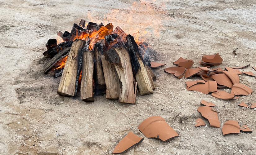 Image of logs on fire with pieces of terra cotta pots on the ground
