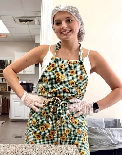 Mikailie Caulder, donning a sunflower apron and hairnet, is prepared to serve lunch
