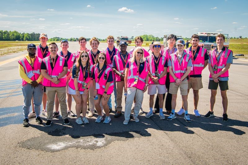 Airport Operations class stands at Auburn airport wearing pink safety vests
