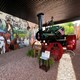 Steam tractor standing in pavilion where agricultural collage mural is displayed on wall
