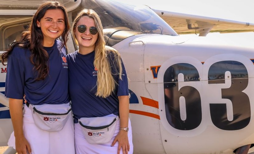 Ashley Baldwin and Meg Cooper stand in front of the Team 63 Skyhawk airplane