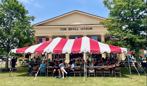 A tent covers tables of festival goers in front of the Tom Bevill Lyceum