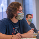 Two students wear face masks in a classroom with text reading COVID plus speech clarity, the masked speaker